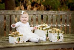 baby girl sitting on bench at morris county park in NJ opening gifts for holiday 