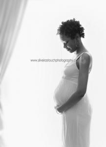 pregnant mom pictured in front of window light holding belly