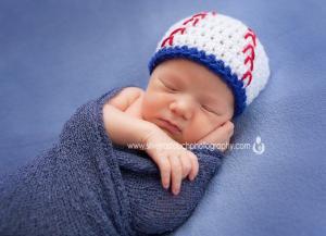 newborn boy sleeping on blue blanket wearing baseball hat