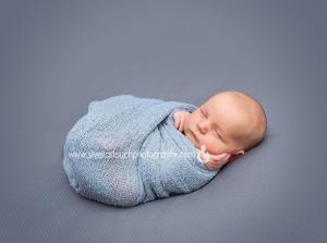 newborn boy sleeping wearing a light grey mesh wrap