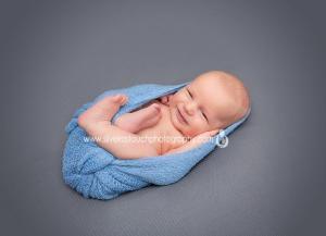 chunky newborn boy photos wrapped in blue blanket smiling