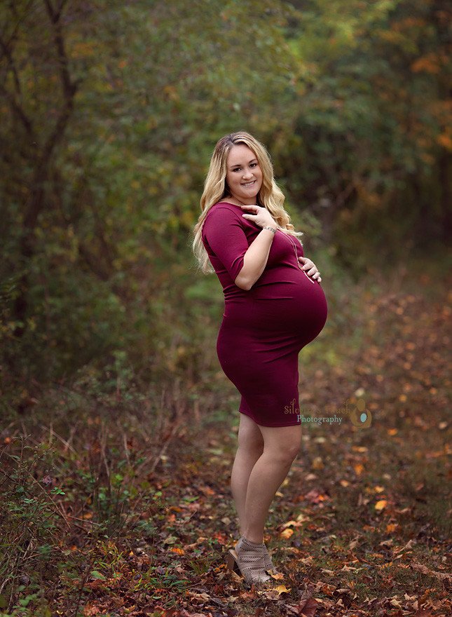 mom to be wearing red maternity dress in the woods