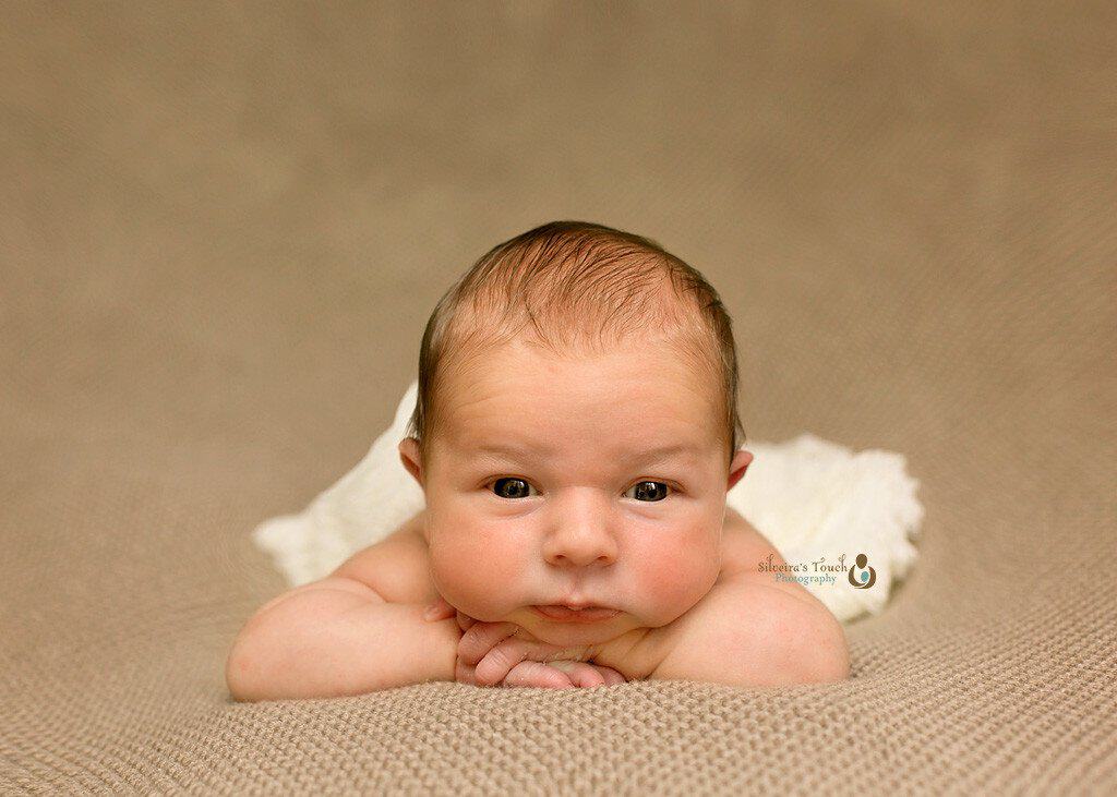 Newborn Photography of baby boy laying on cream backdrop looking at camera