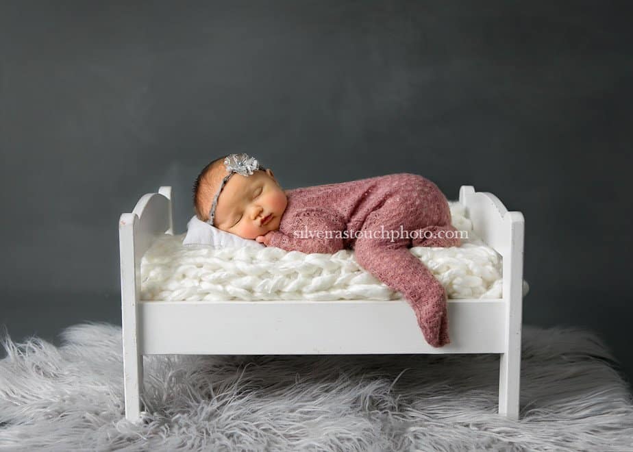 Professional newborn photographer baby on bed posed