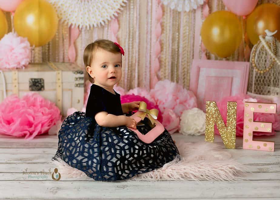 Cake smash photography of baby girl in blue dress smiling with Babydream backdrop decoration