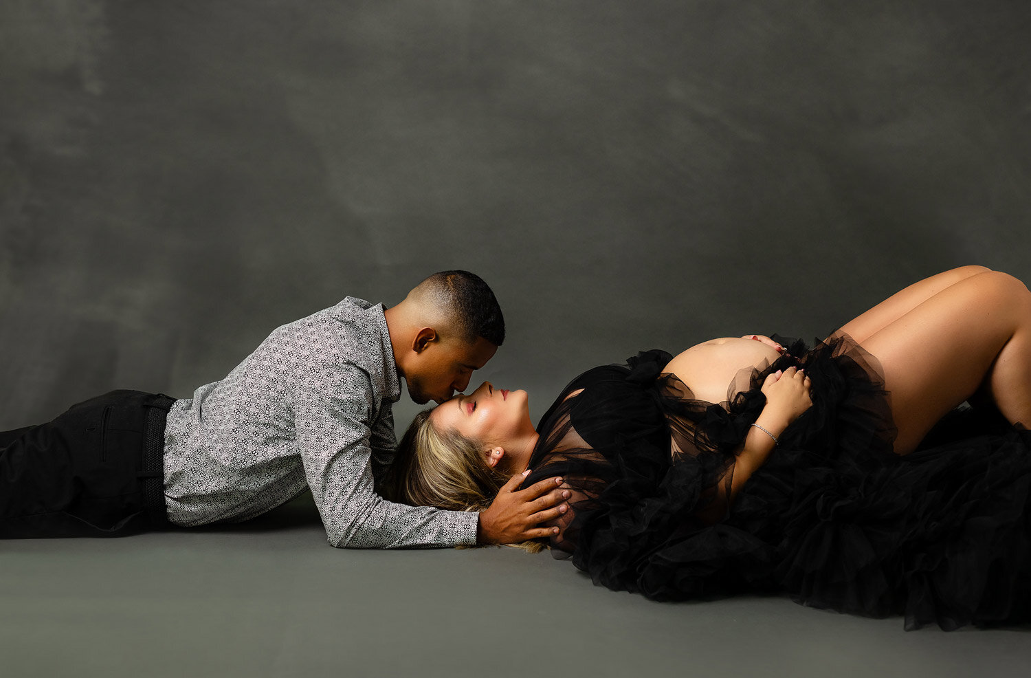 couples maternity session in studio of dad kissing mom forehead wearing black gown