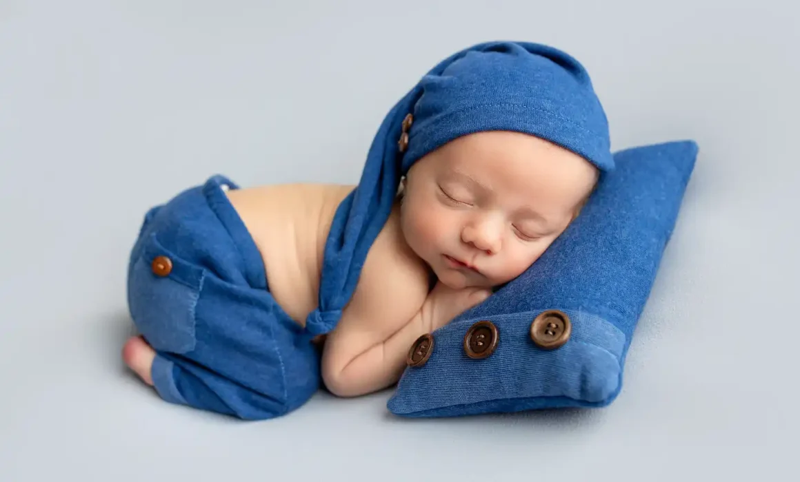 newborn baby boy wearing blue sleeper cap posed on blue blanket in long valley studio