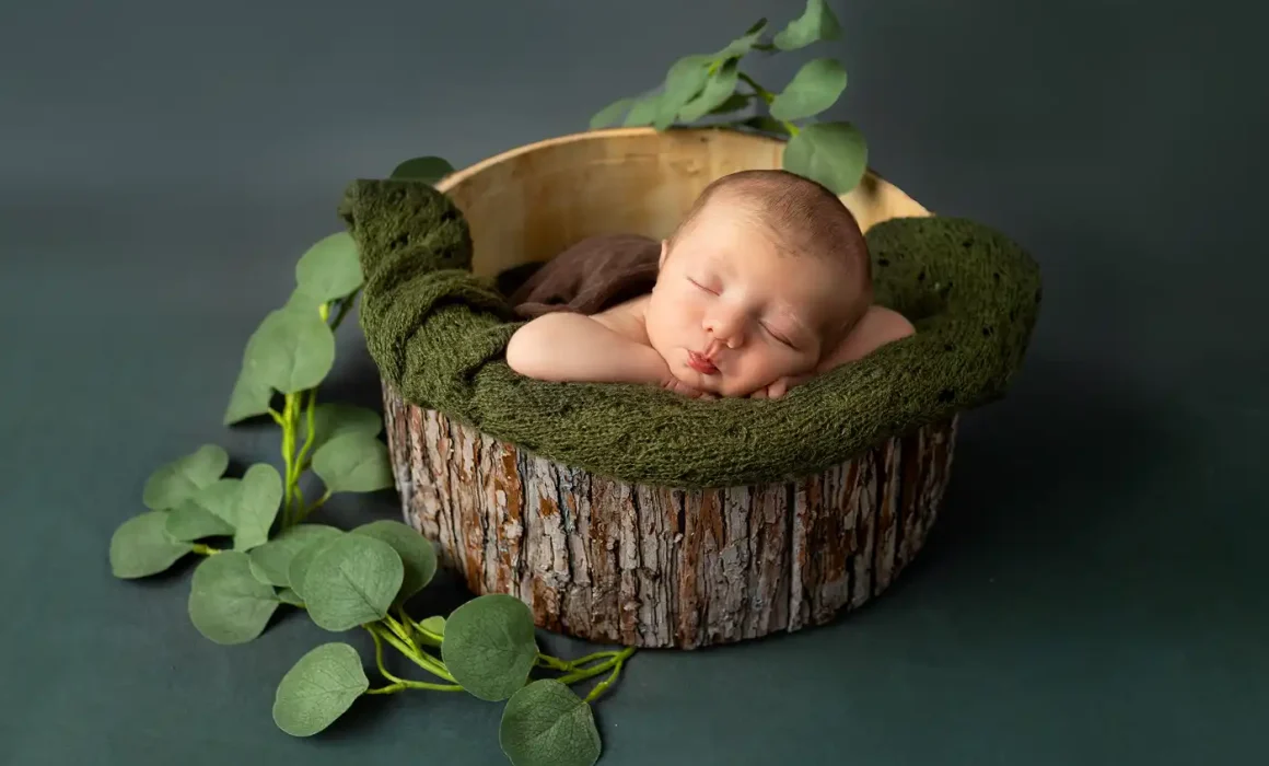newborn photographed in tree trunk bucket with green blanket lips puckering