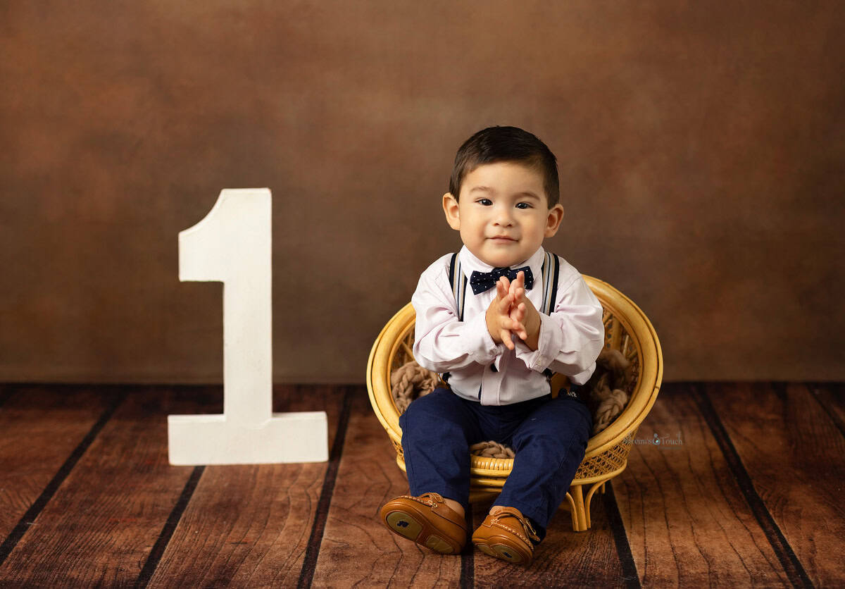 baby boy clapping sitting on little chair for his first birthday photos