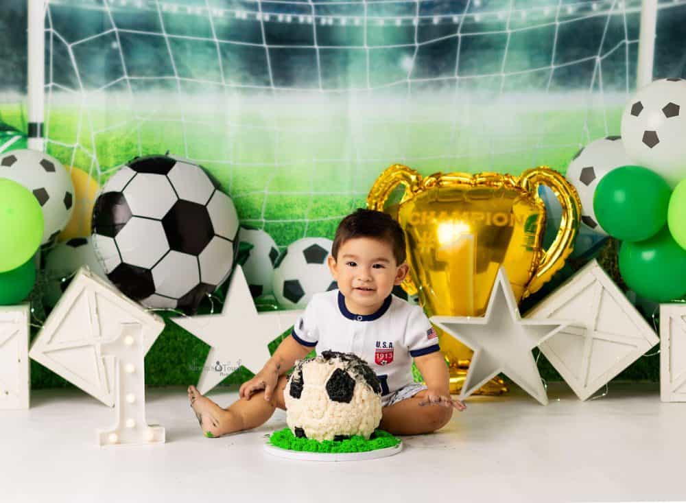 Baby boy smiling in front of soccer ball cake for his soccer themed cake smash session in Randolph NJ