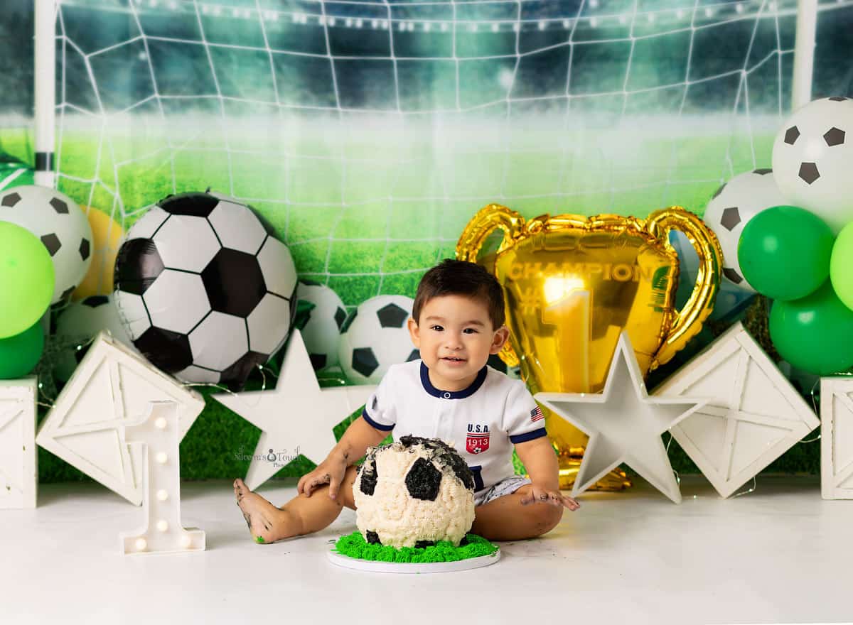 baby boy cheerful giggling in front of his soccer ball cake during his photo shoot