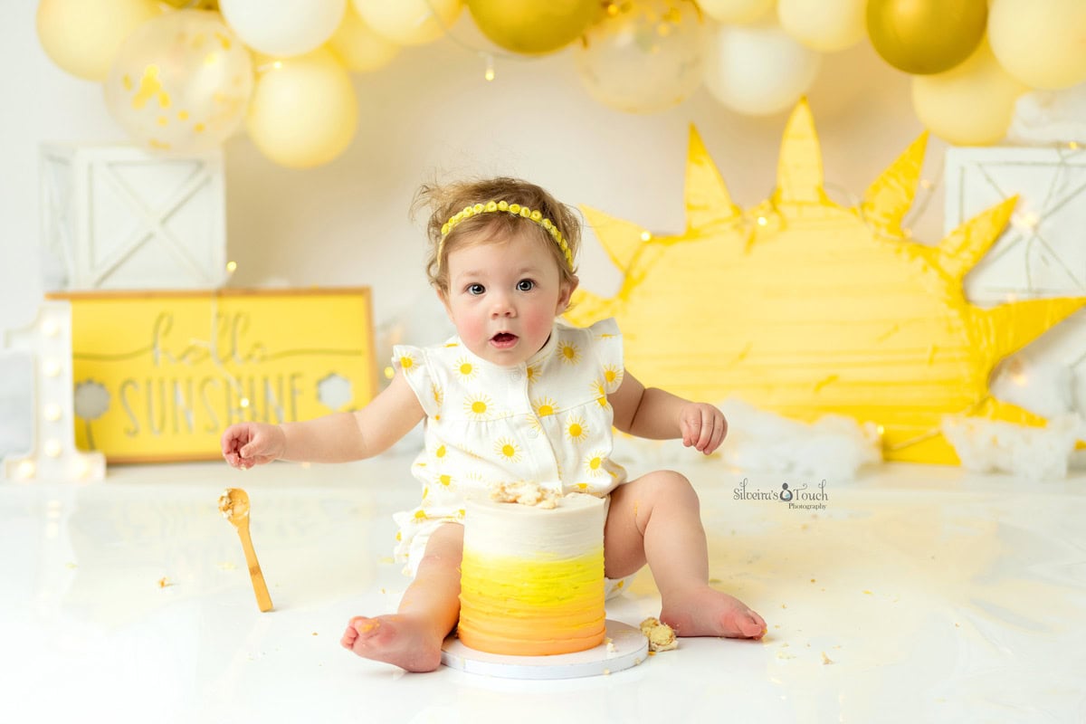 first birthday photoshoot sunshine theme of baby holding spoon to eat her cake